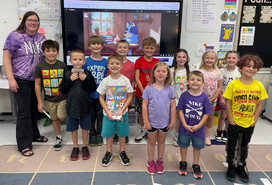 Group of elementary students posing with their teacher in a classroom.