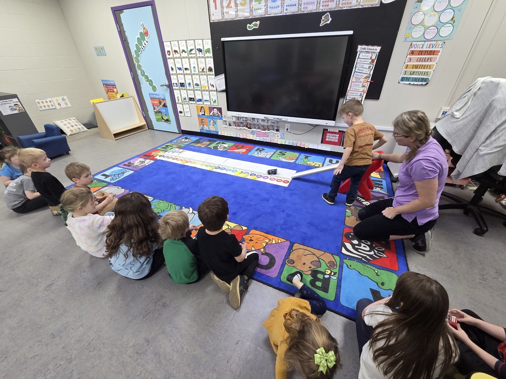 Preschool students sitting around a blue rug in classroom playing a game.