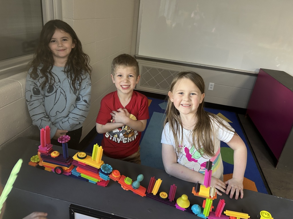 Three preschool students posing for a photo with building blocks.