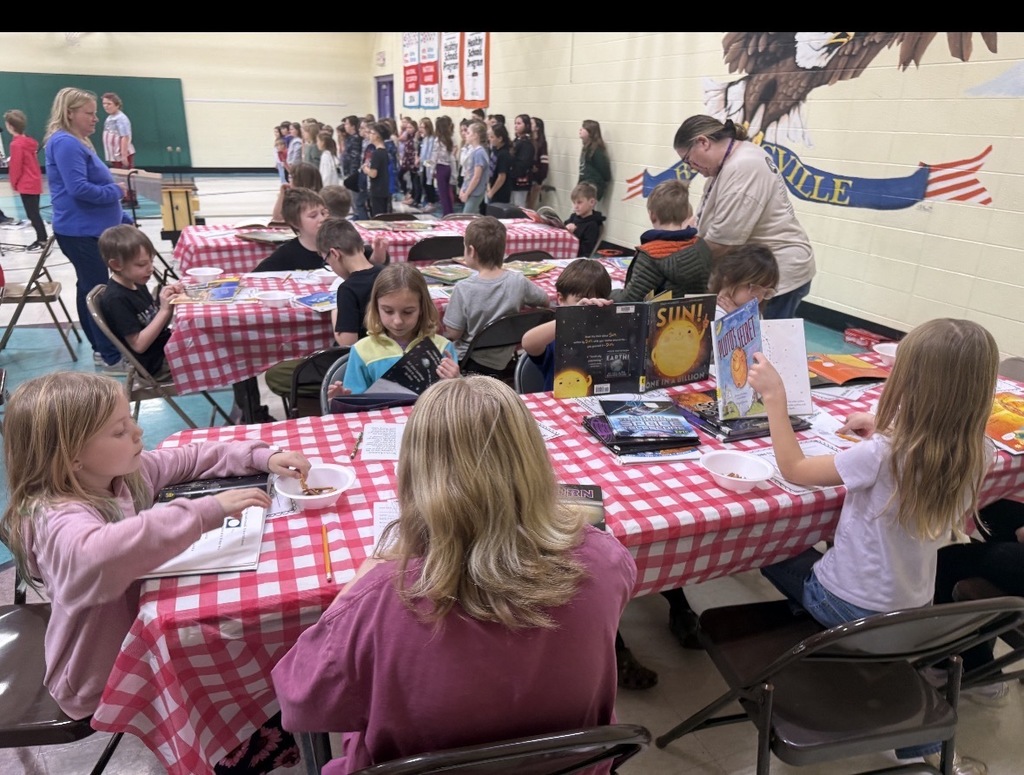 Students in a small gym at tables reading various books. 