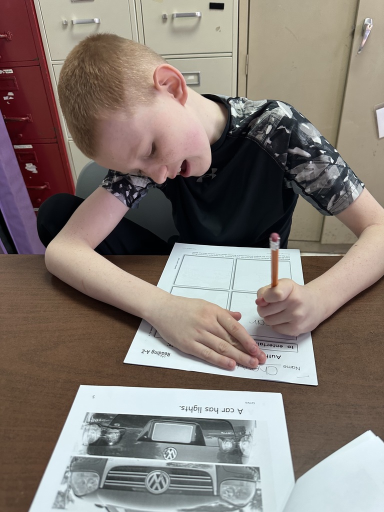 Student leans over a desk, writing on a worksheet with a pencil during a classroom activity.