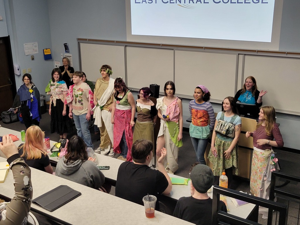 Group of students dressed in various costumes in front of a classroom of students.