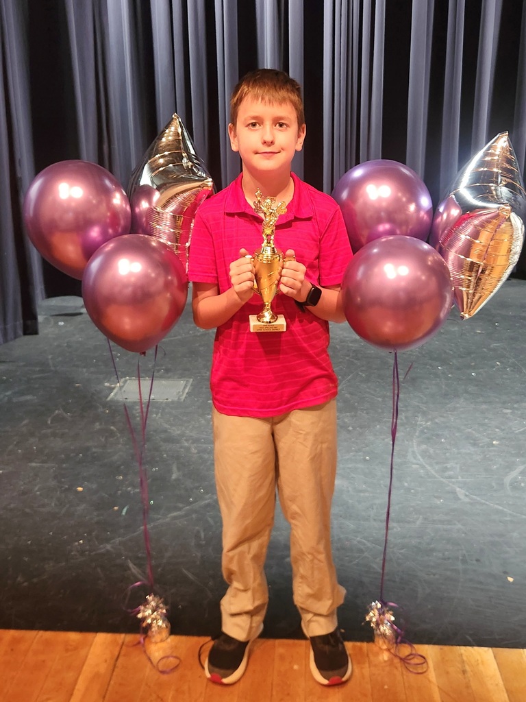 Male student holding a gold trophy surrounded by pink and silver balloons.