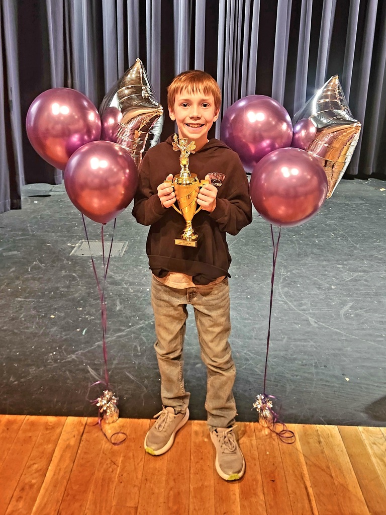 Male student holding a gold trophy surrounded by pink and silver balloons.