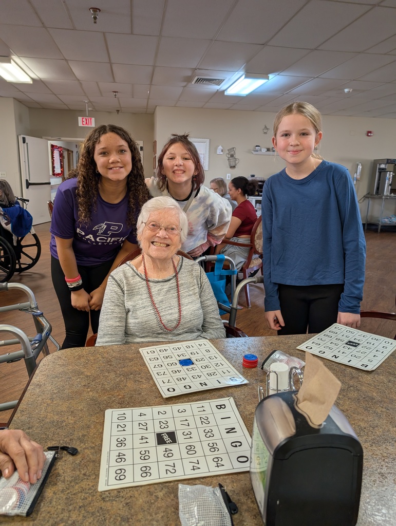 Three students and a resident posing together around a table with bingo cards on it.
