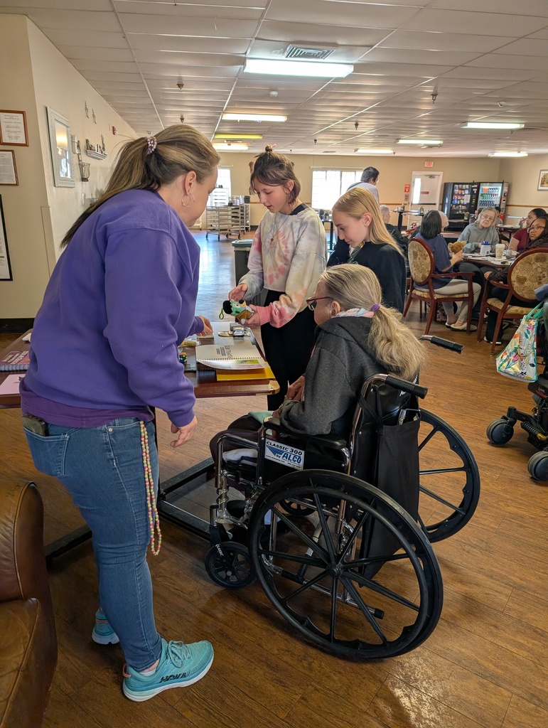 Staff member and students helping a resident in a wheelchair gather materials from a table.