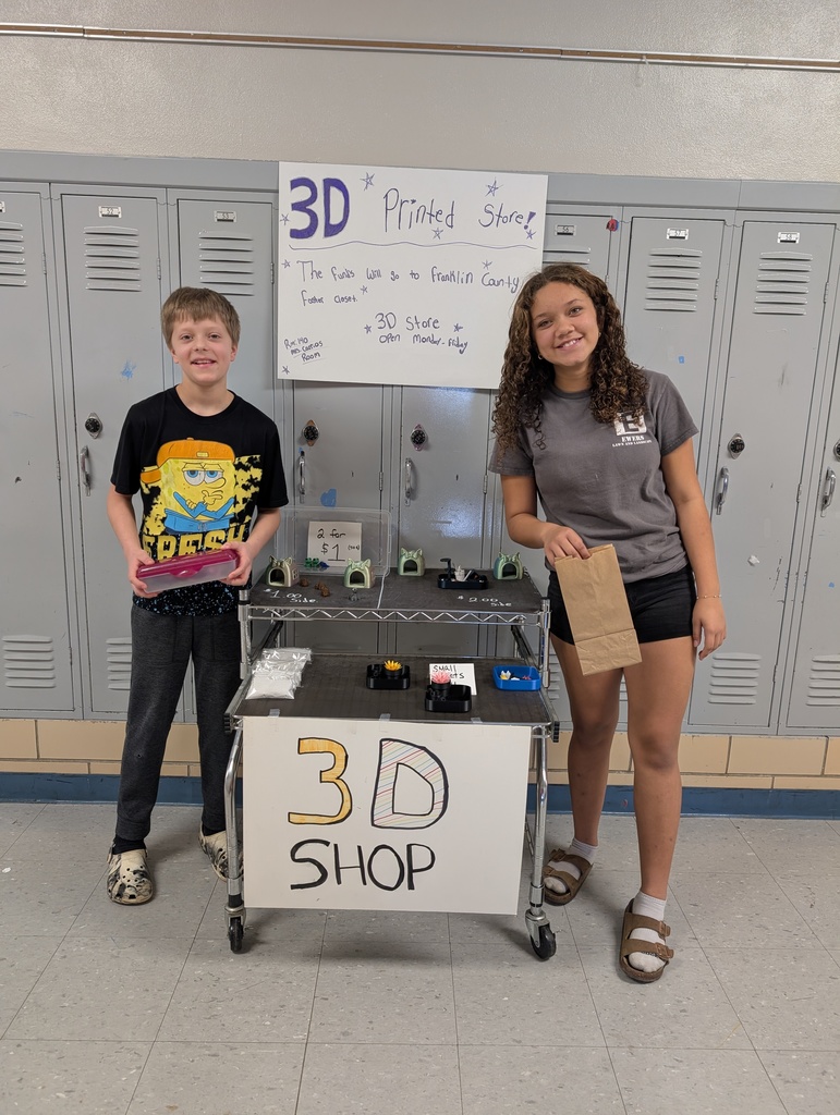 Two students posing in front of a 3D shop cart. 