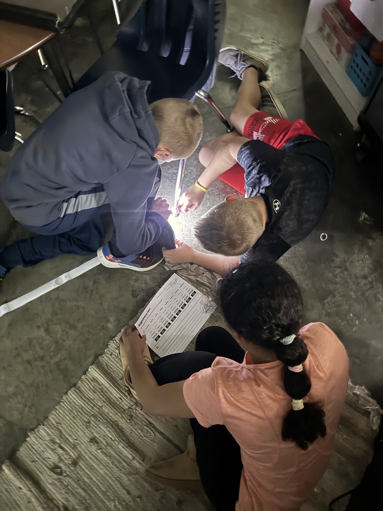 Three students using a flashlight in a school classroom.