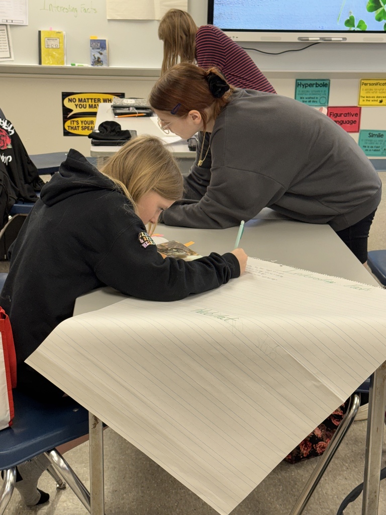 Two students writing on two large pieces of paper.