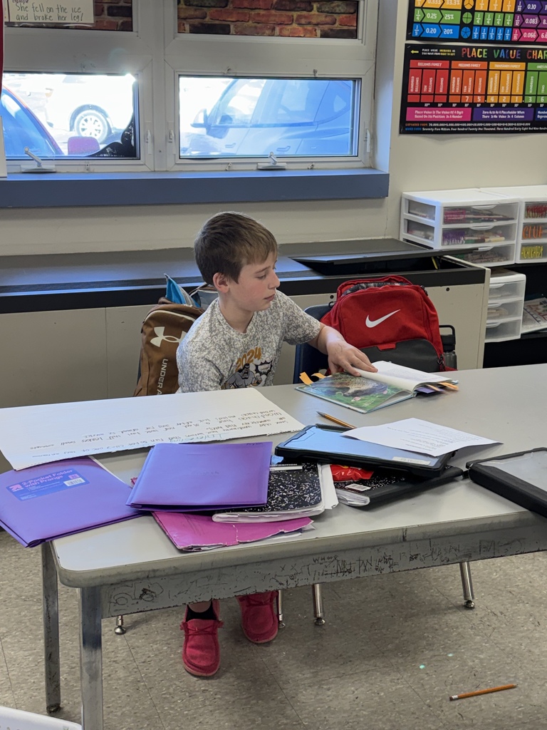 Student reading a book at a desk with various notebooks spread across it.