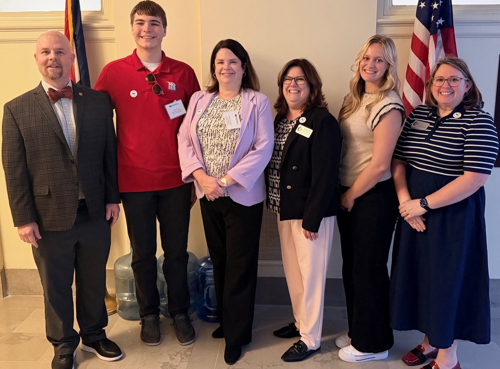Group photo of students and board members standing in front of two flags.