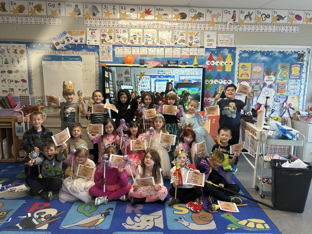 Group of students in a classroom holding papers and dressed as kings and queens.