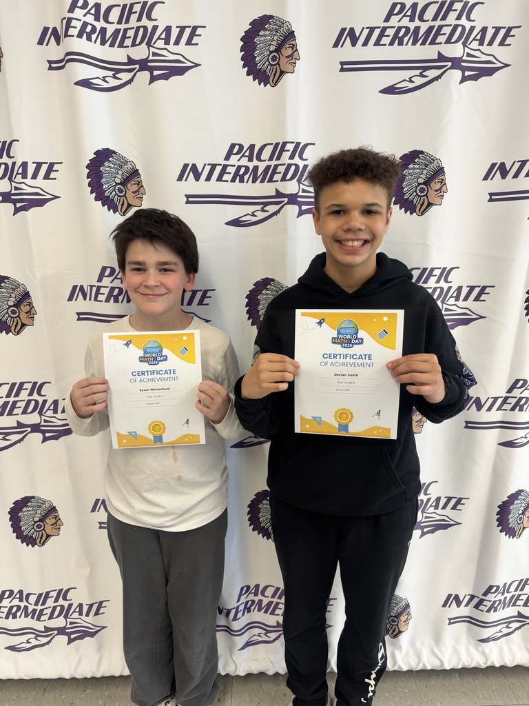 Two students standing in front of a Pacific Intermediate banner holding certifications of achievement. 