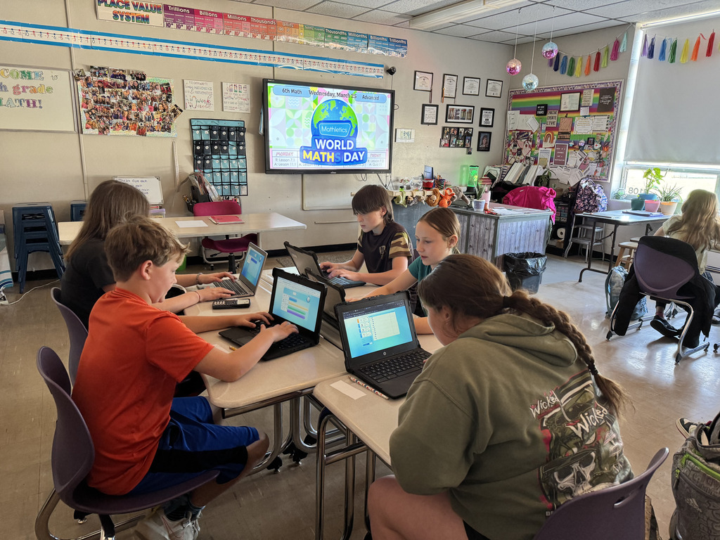 Students working on laptops at their desks in a dim lit classroom.