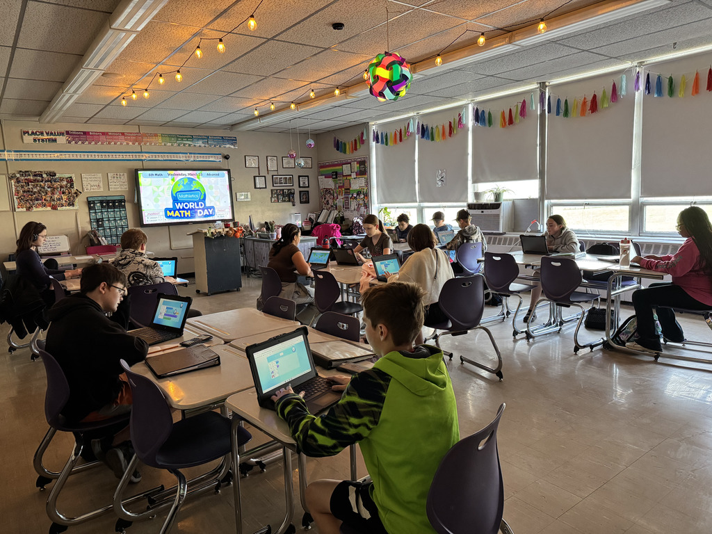 Students working on laptops at their desks in a dim lit classroom.