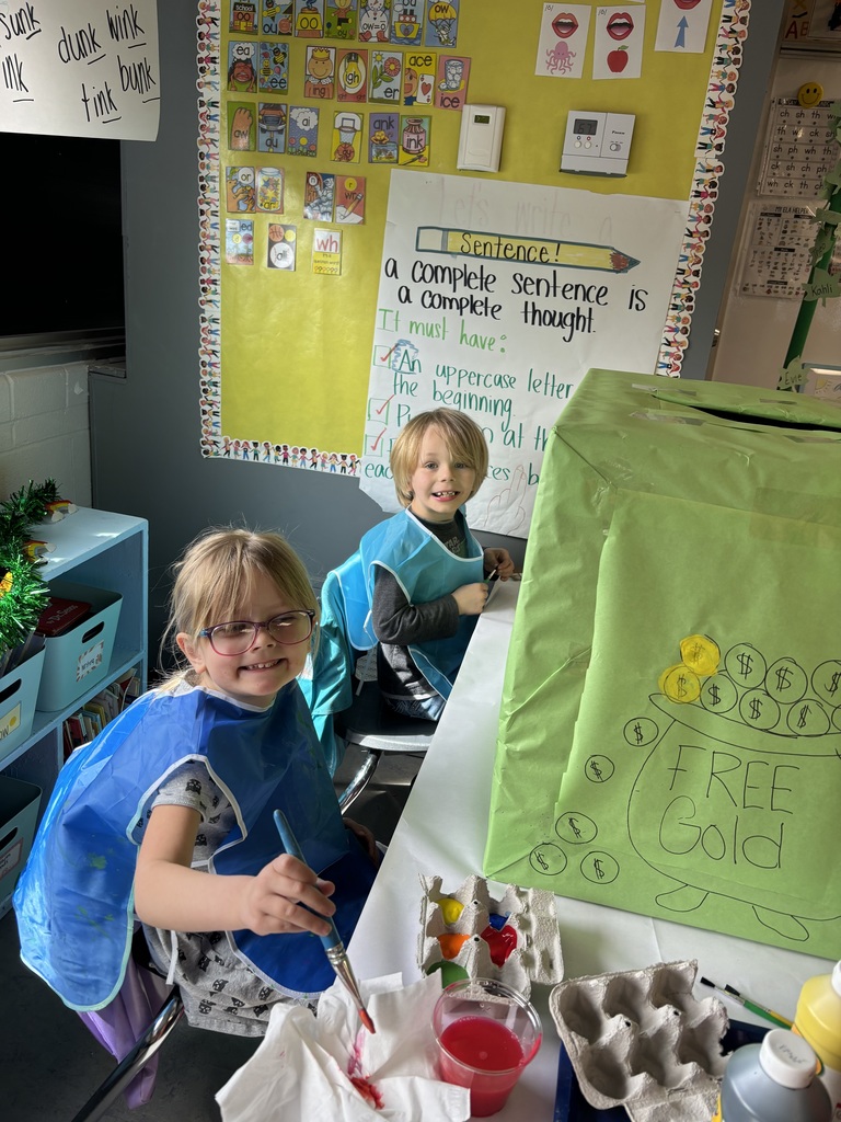 Two students smiling for a photo while working on a painting activity.