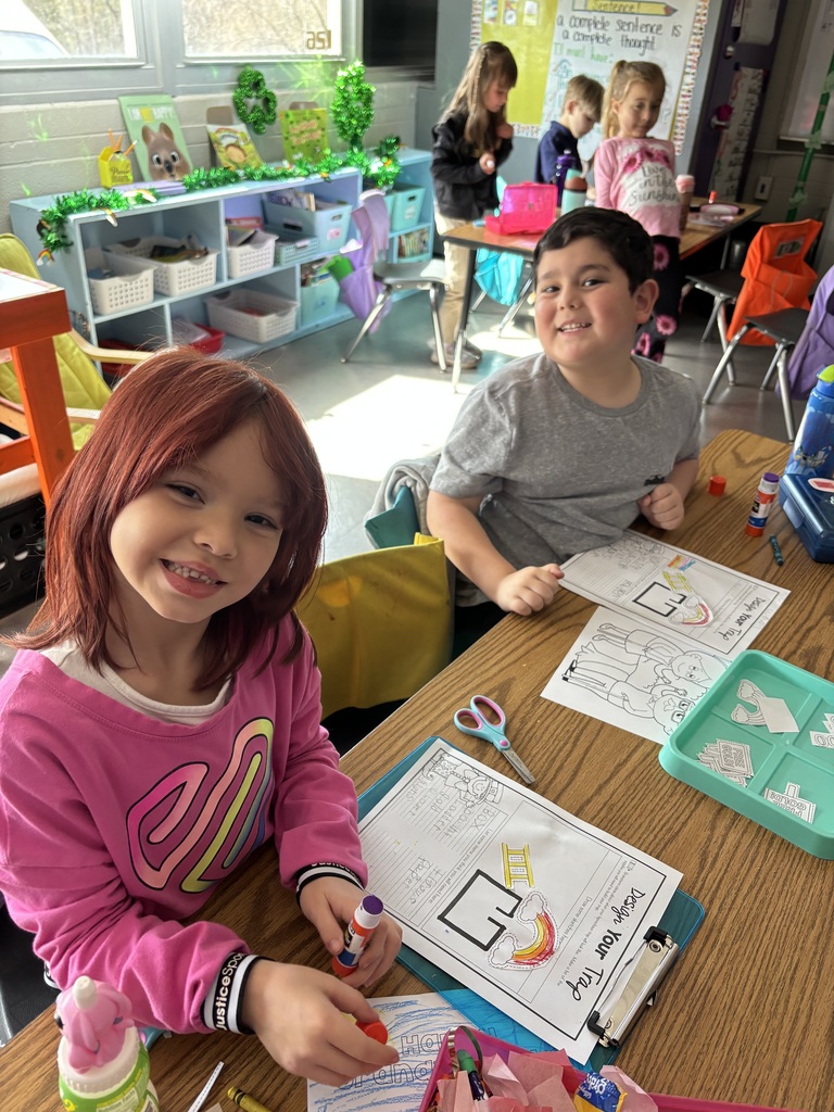 Two students smiling for a photo while working on gluing worksheets.
