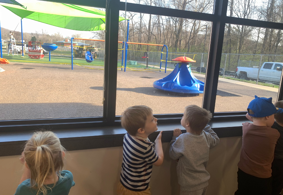 Students in a classroom looking at a playground through the window.