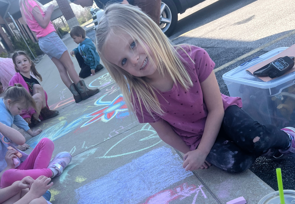 Students smiling next to chalk artwork on the sidewalk.