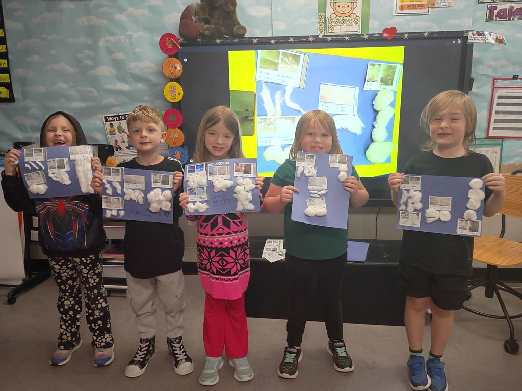 Students posing with various artwork in an elementary clasroom.