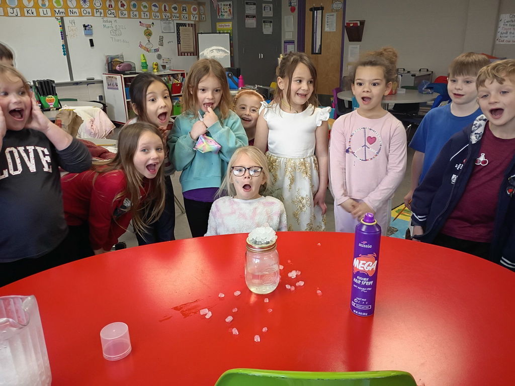 Students sharing a shocked expression while looking at a science experiment on a red desk.