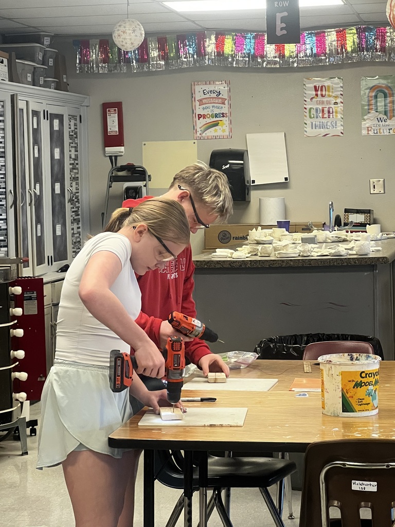 Two students using tools in the classroom on pieces of wood.