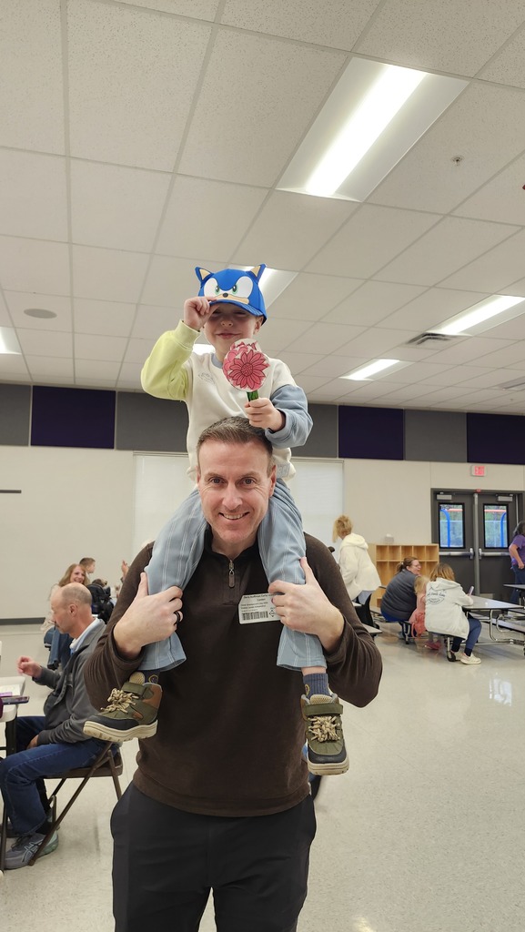A young student wearing a blue hat sitting on an adults shoulders, both smiling.