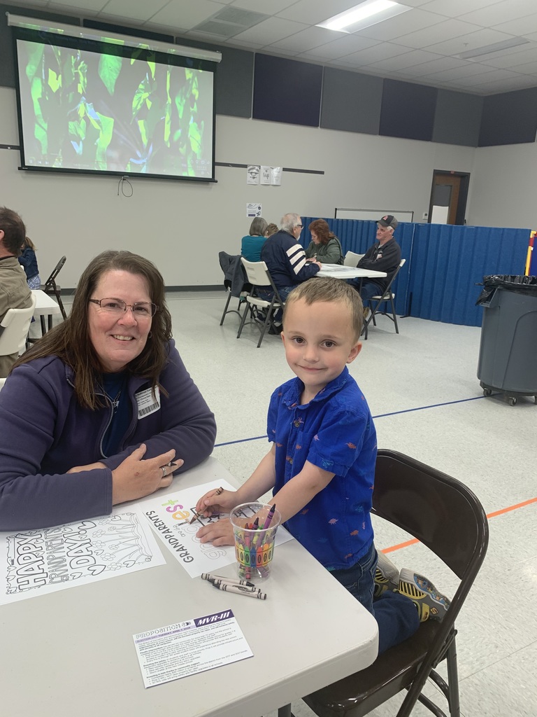 Student and adult coloring a worksheet at a table in a gym.