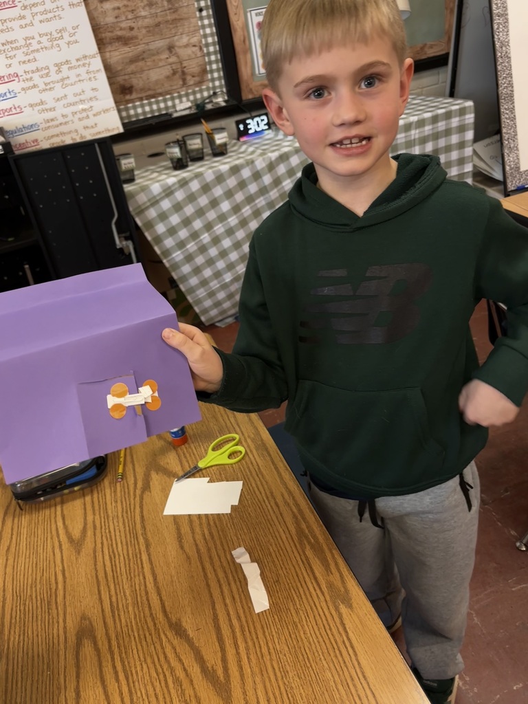 Young student showing their purple paper assignment while smiling. 