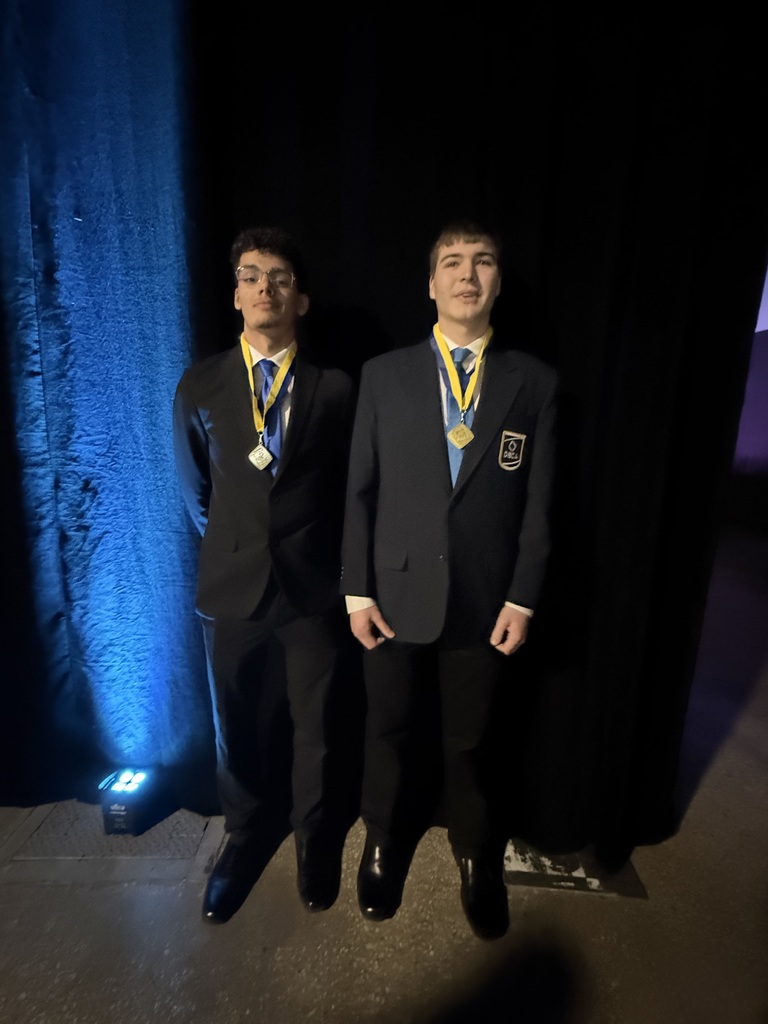 Two male students wearing black suits with blue and yellow medals around their necks.