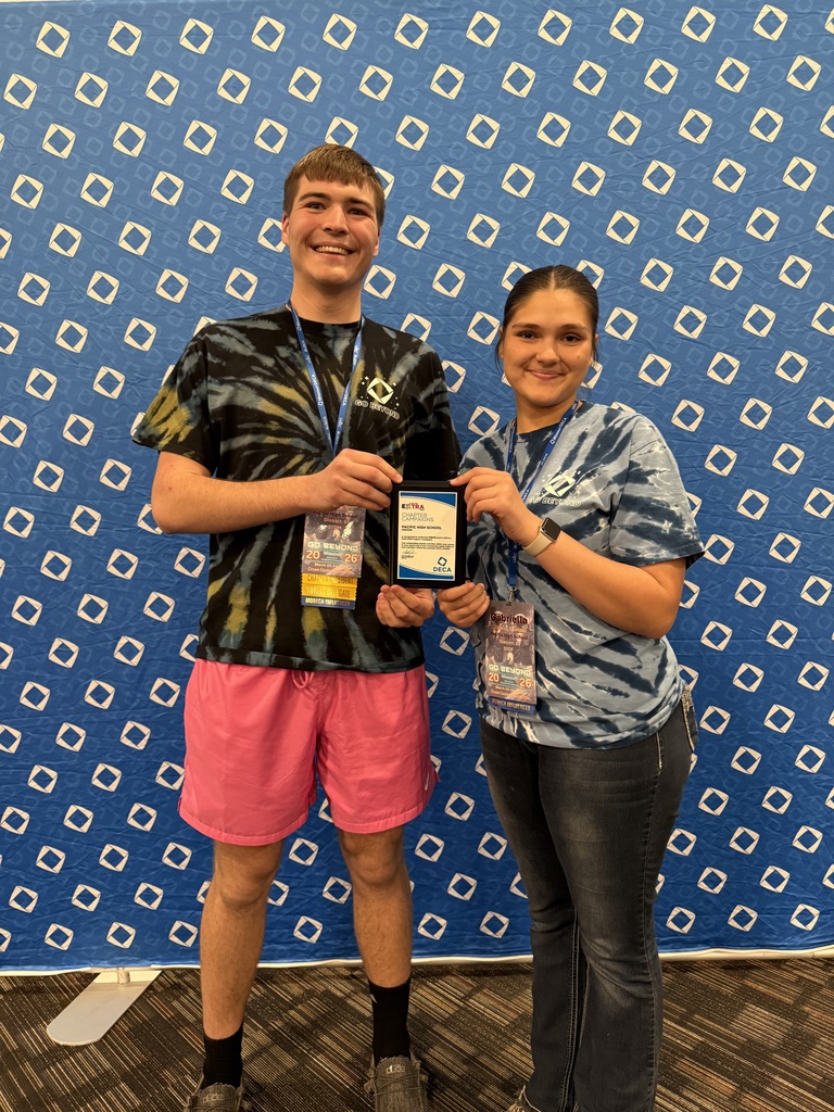Two students holding a small plaque in front of a large blue banner.