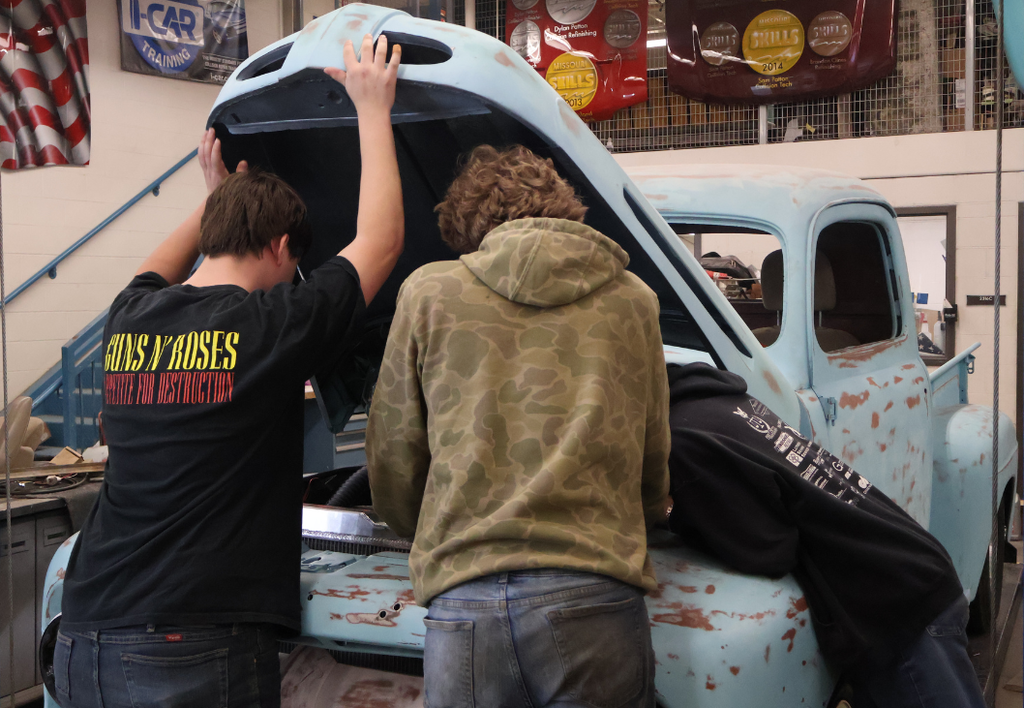 Three students working on an old blue truck. 