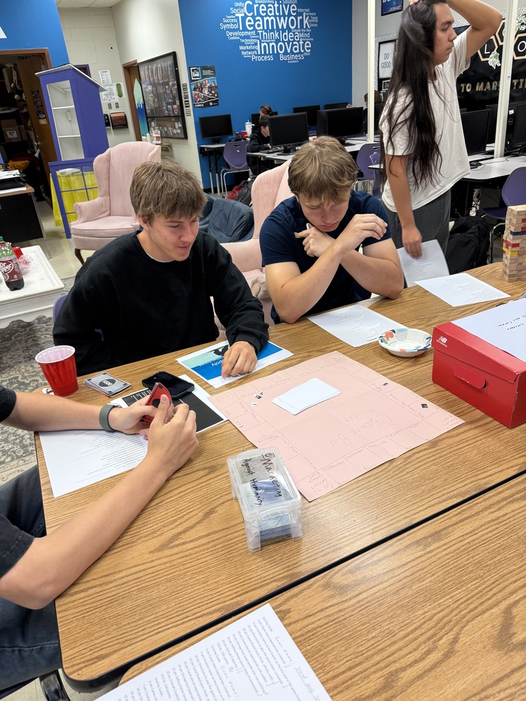 Students playing a game with a large pink piece of paper at a school desk.