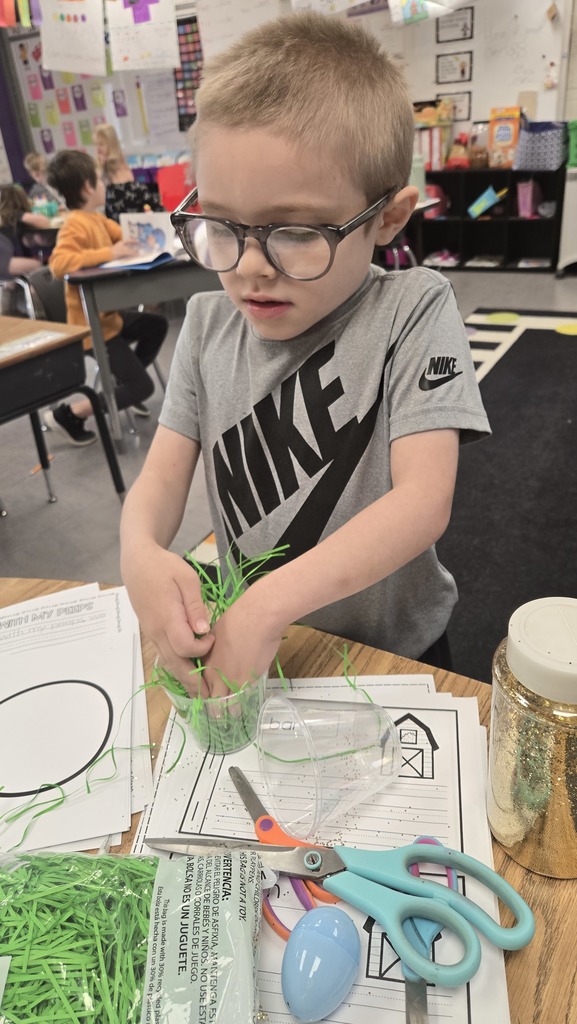 Young student putting green shredded paper into a small plastic cup.