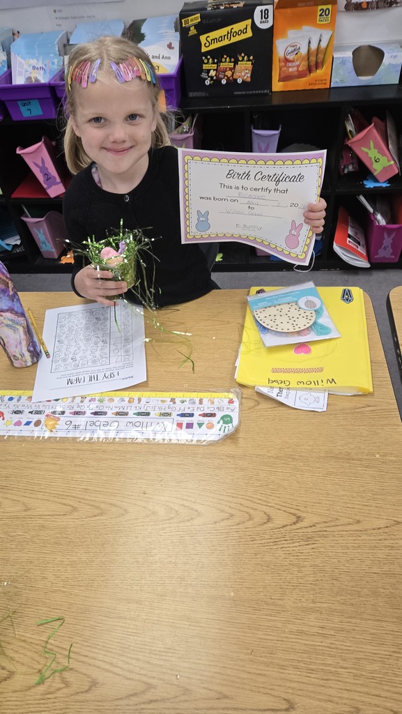 Young student showing a colorful piece of paper at a classroom desk.