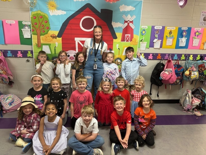 Group students and teacher dressed in farm clothes posing in front of a barn banner.