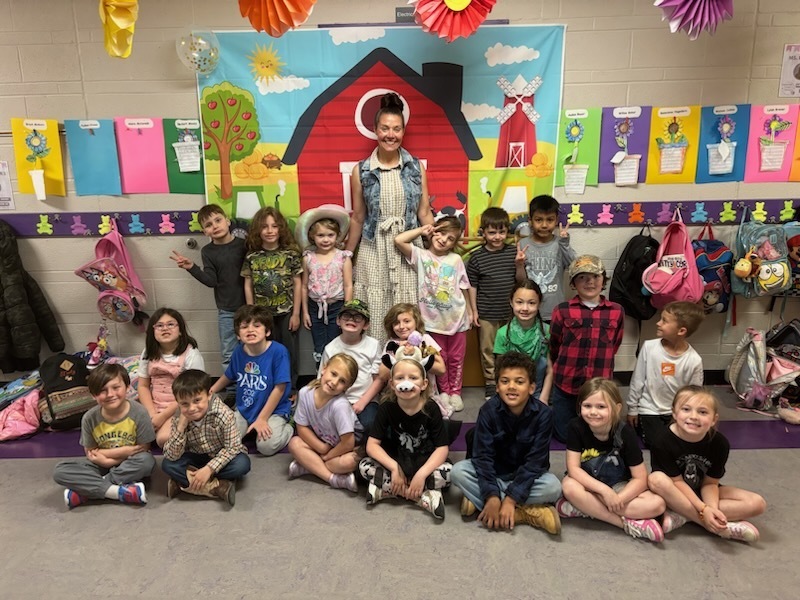 Group students and teacher dressed in farm clothes posing in front of a barn banner.