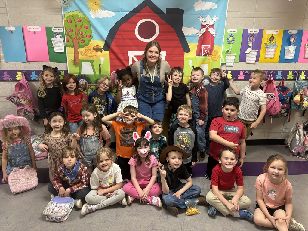 Group students and teacher dressed in farm clothes posing in front of a barn banner.