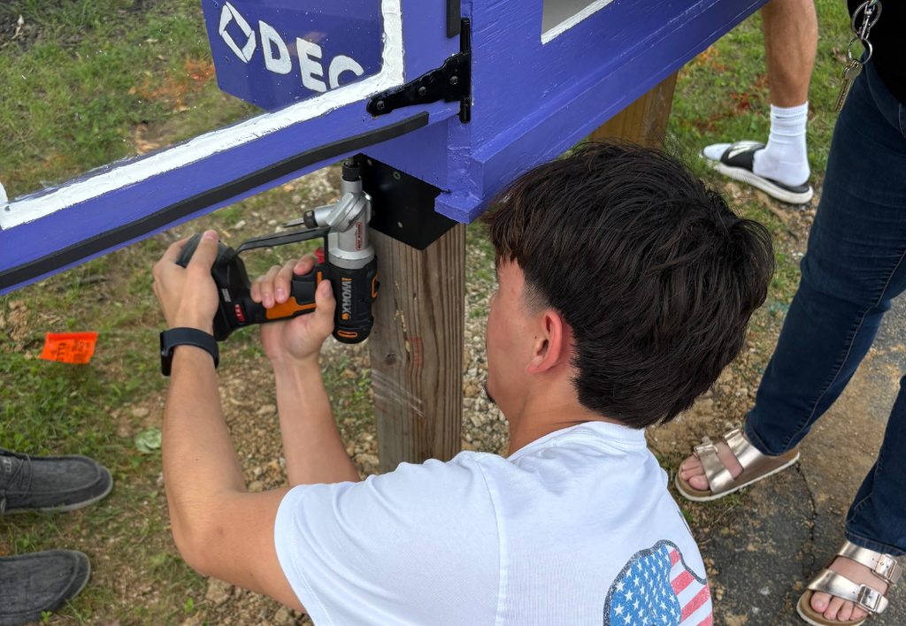 Student using a drill to work on a wood project outdoors.