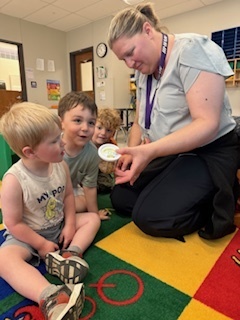 Two students with wow faces as a teacher shows them a caterpillar.