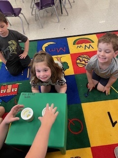 Three students with wow faces as a teacher shows them a caterpillar.