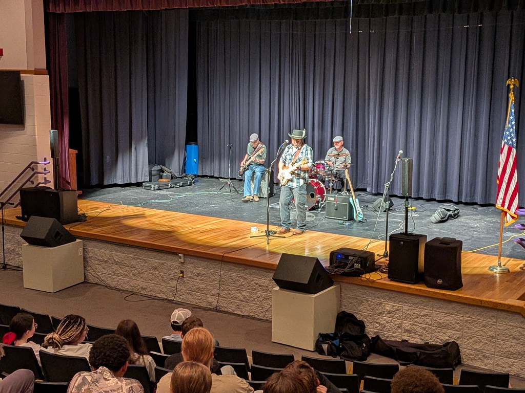 Three band members performing on a black and wooden stage.