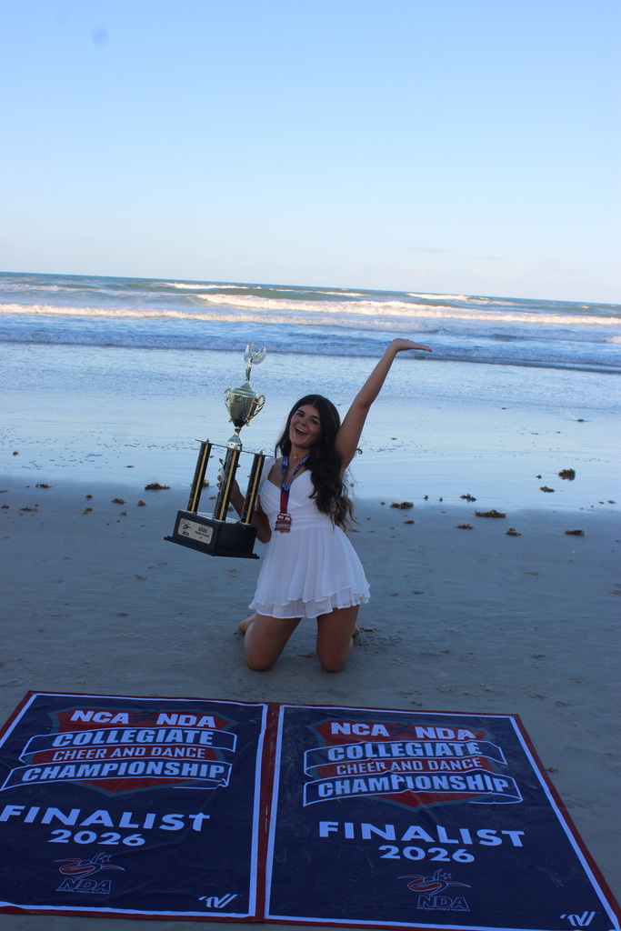 Maria Signaigo posing on a beach, holding a trophy, with 2026 NCA & NDA Collegiate Cheer and Dance Championship Finalist banners.
