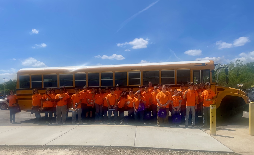 A large group of students pose outdoors in front of a school bus.
