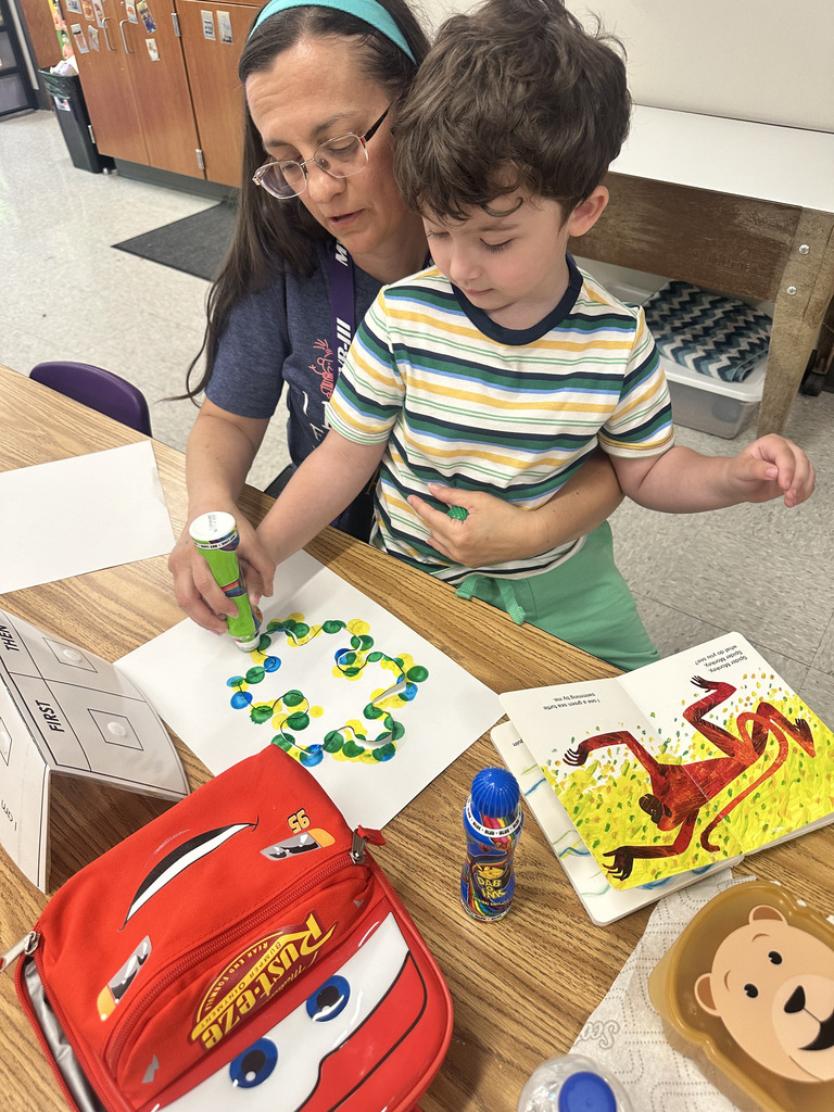 A teacher helps a young student use a colorful ink dotting pen on a sheet of paper.