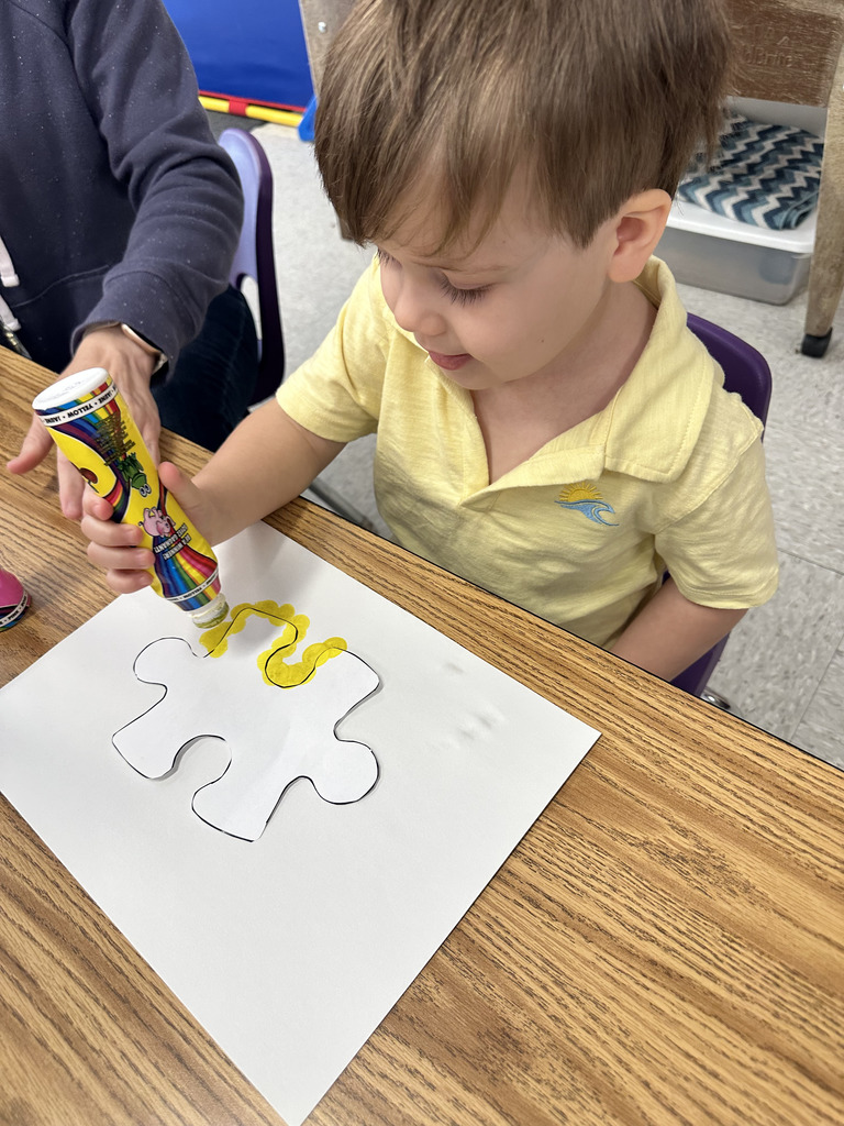 A student uses a yellow marker to trace a puzzle piece on a sheet of paper.