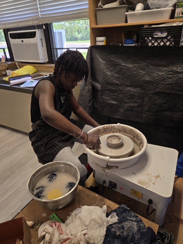 A student wears an apron and spins clay.