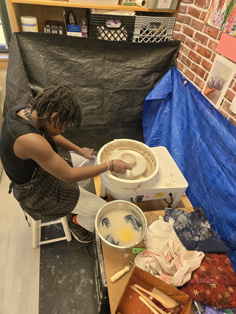 A student wears an apron and spins clay.