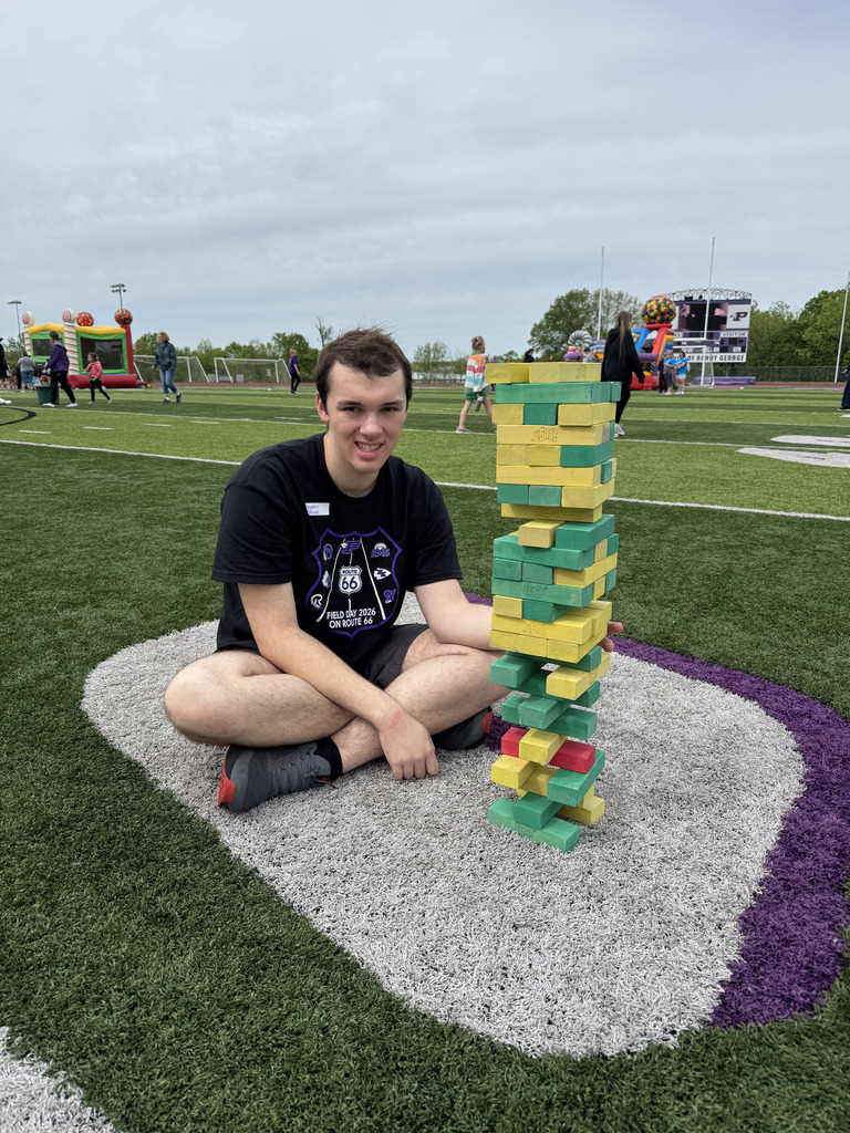 Student sitting beside a tower of blocks on a football field.