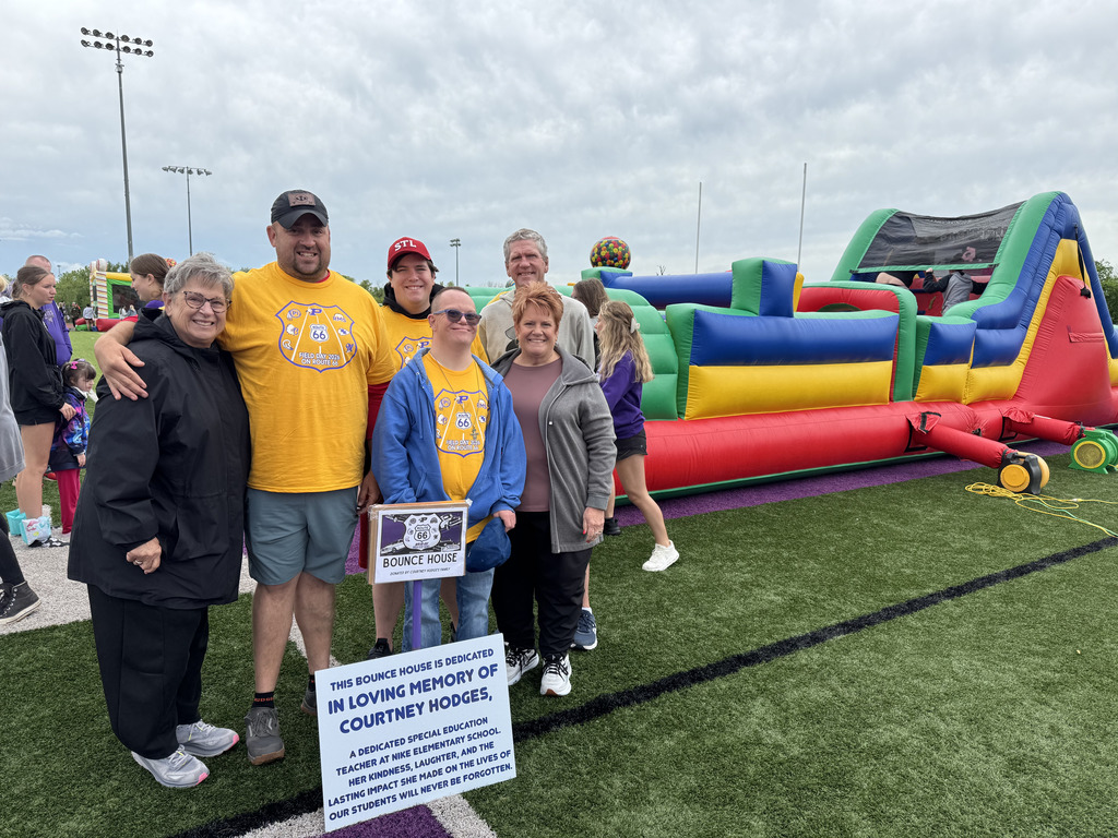Adult group standing in front of a large bounce house with a poster, "In loving memory of Courtney Hodges."